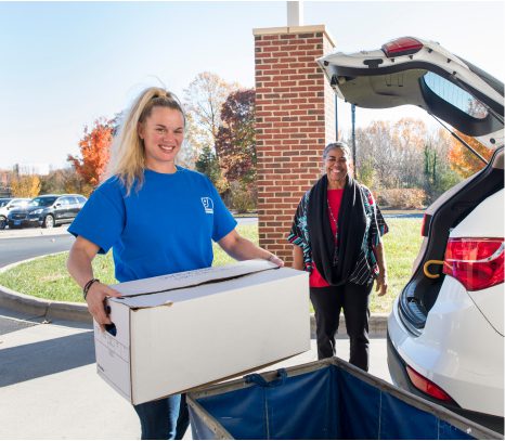 Women unloads a box from the back of an elderly woman's white suv trunk